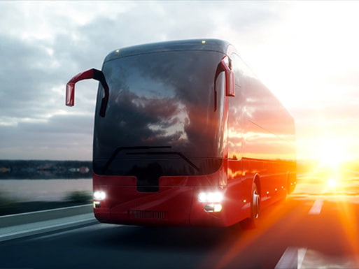 a red charter bus drives on a road at sunset