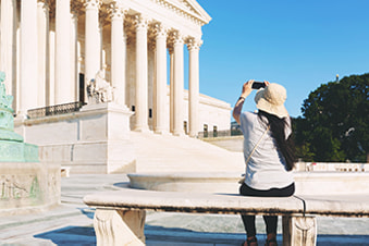 A woman with a camera sits in front of the Lincoln Memorial in Washington D.C.